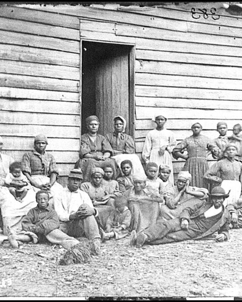 Period photograph of a group of formerly enslaved African American men, women, and children gathered outside a farmhouse during the Civil War.